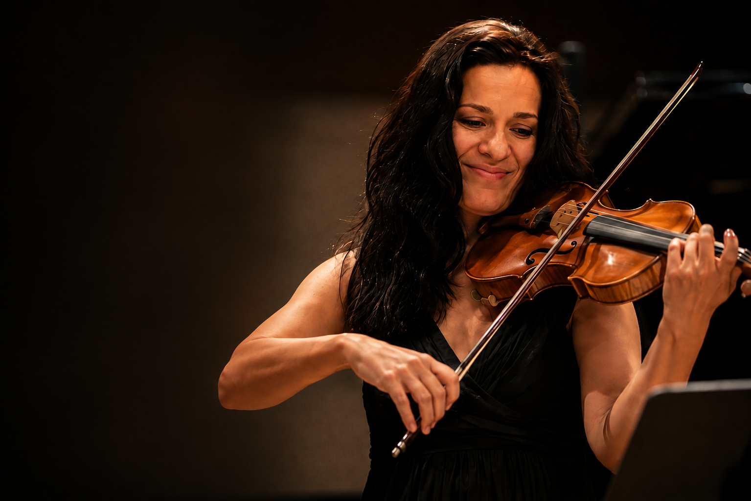Stanislava performing violin in a black concert dress under warm stage lights